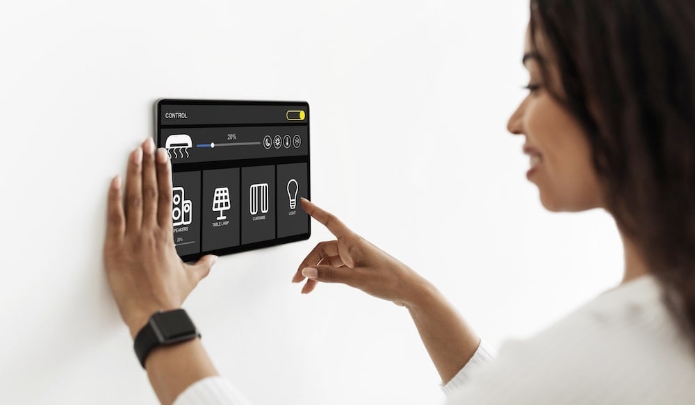 女子在牆上觸控面板操作智能家居設備，包括燈光、窗簾與音響