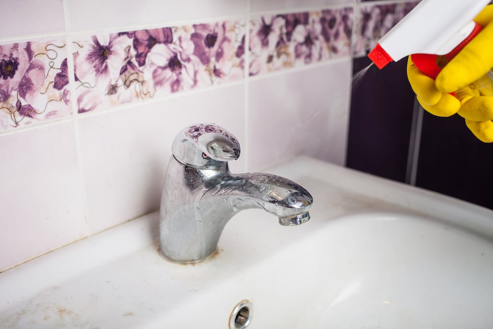 浴室水龍頭被水垢和水漬覆蓋，正在使用清潔劑進行水垢清潔