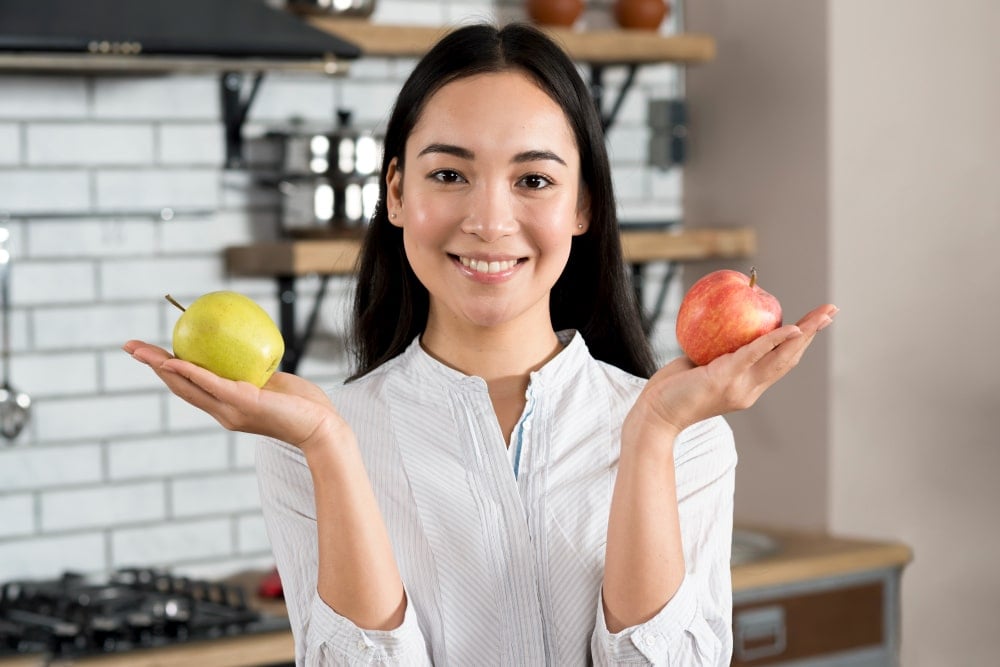 止咳方法 年輕女性在廚房中手持蘋果,展示天然食療止咳方法,透過水果與營養增強免疫力。